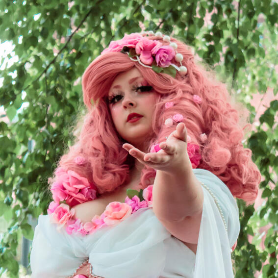 Girl with pink curly hair reaching out hand with trees in background